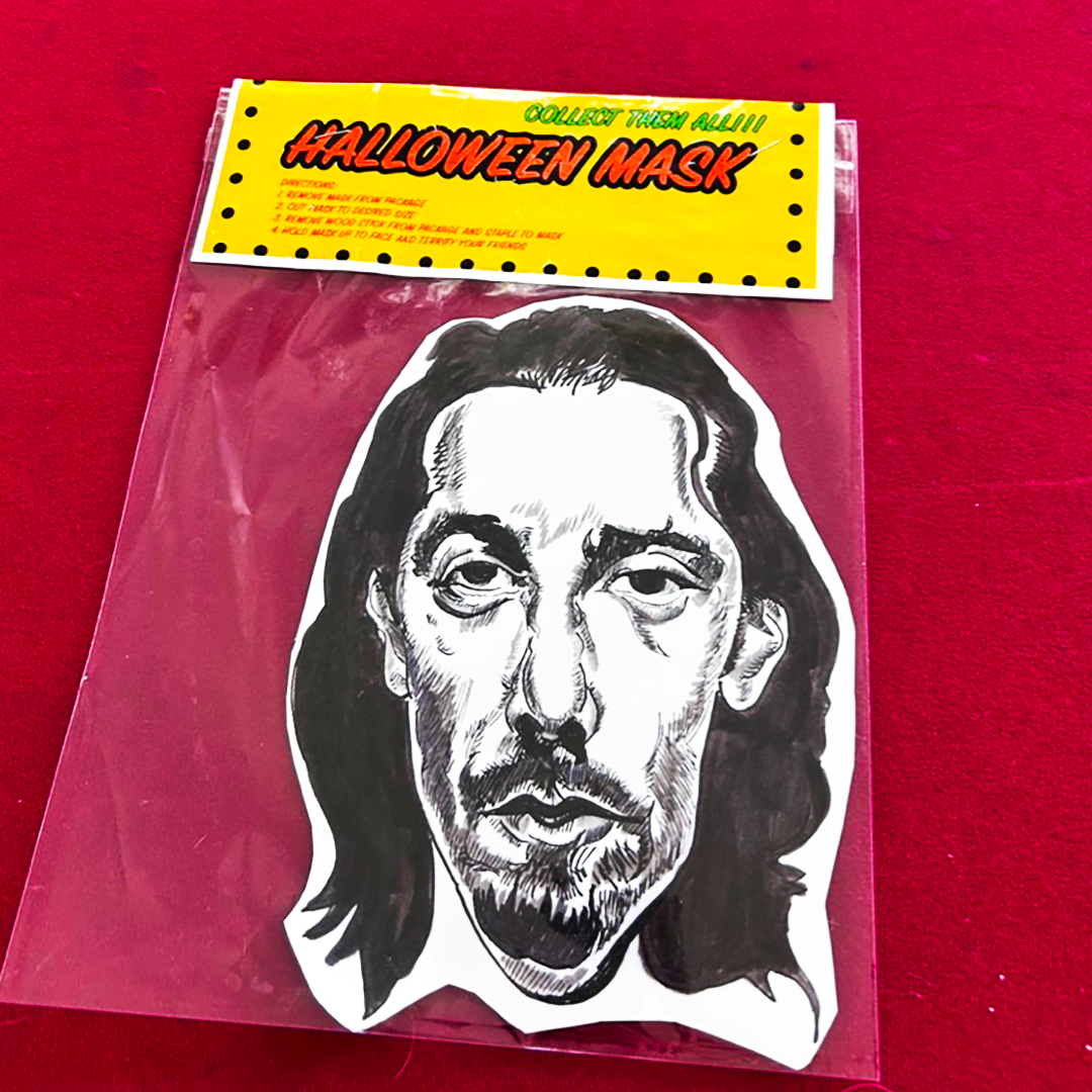 Paul Reubens mugshot Halloween mask in clear packaging and yellow hang tag, with a red background